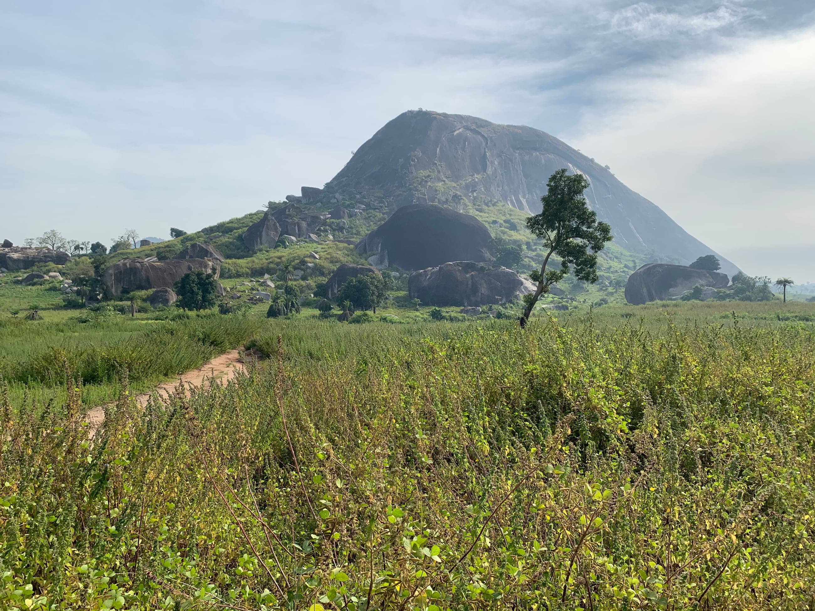 Zuma Rock rising above the green savanna near Abuja, Nigeria, with a footpath leading toward it